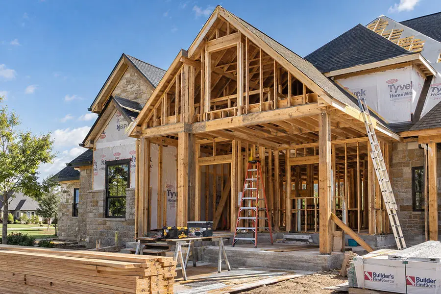 Residential home under construction with exposed wood framing, ladders, tools, and stacked lumber at a North Texas job site. Residential home under construction with exposed wood framing, ladders, tools, and stacked lumber at a North Texas job site.